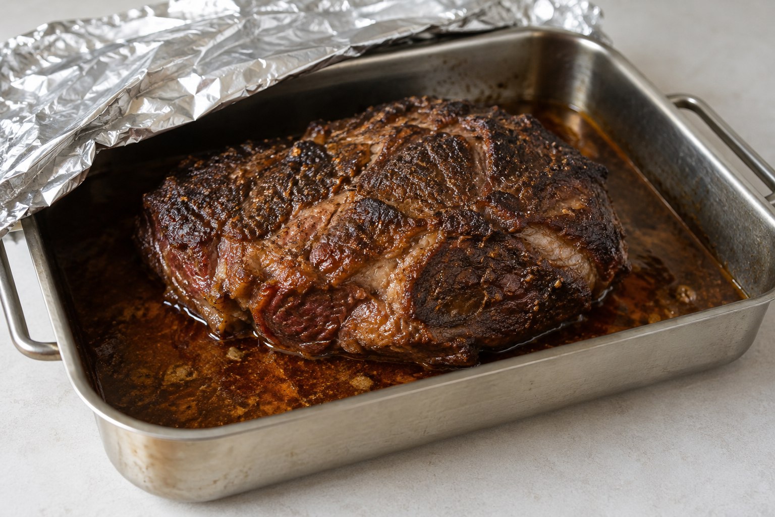 Chuck roast in a shallow pan, foil pulled back.
